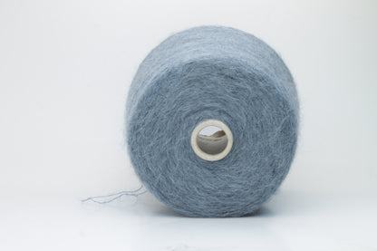 Close-up photograph showcasing a vibrant blue SuperKidMohair yarn skein, displaying a dense, fluffy texture with subtle sheen. The ply twist is evident, revealing a tightly wound thread structure.