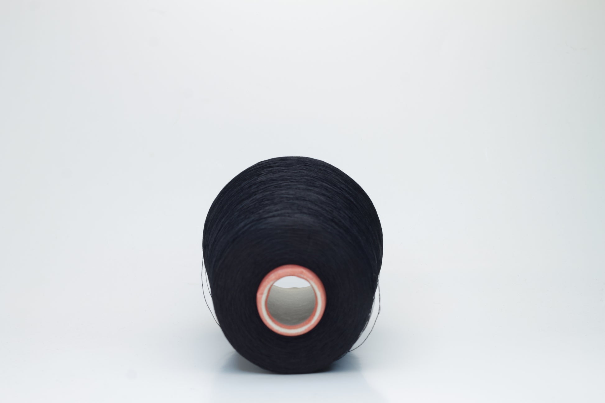 A single, tightly spun strand of incredibly fine, jet black silk yarn, showcasing a brilliant, almost glass-like sheen.