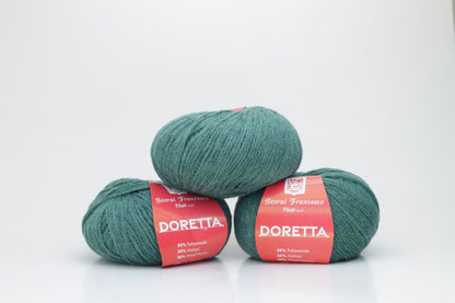 Close-up of a ball of fluffy, vibrant forest green yarn with a visible soft halo, highlighting the luxurious mohair and merino fibers.