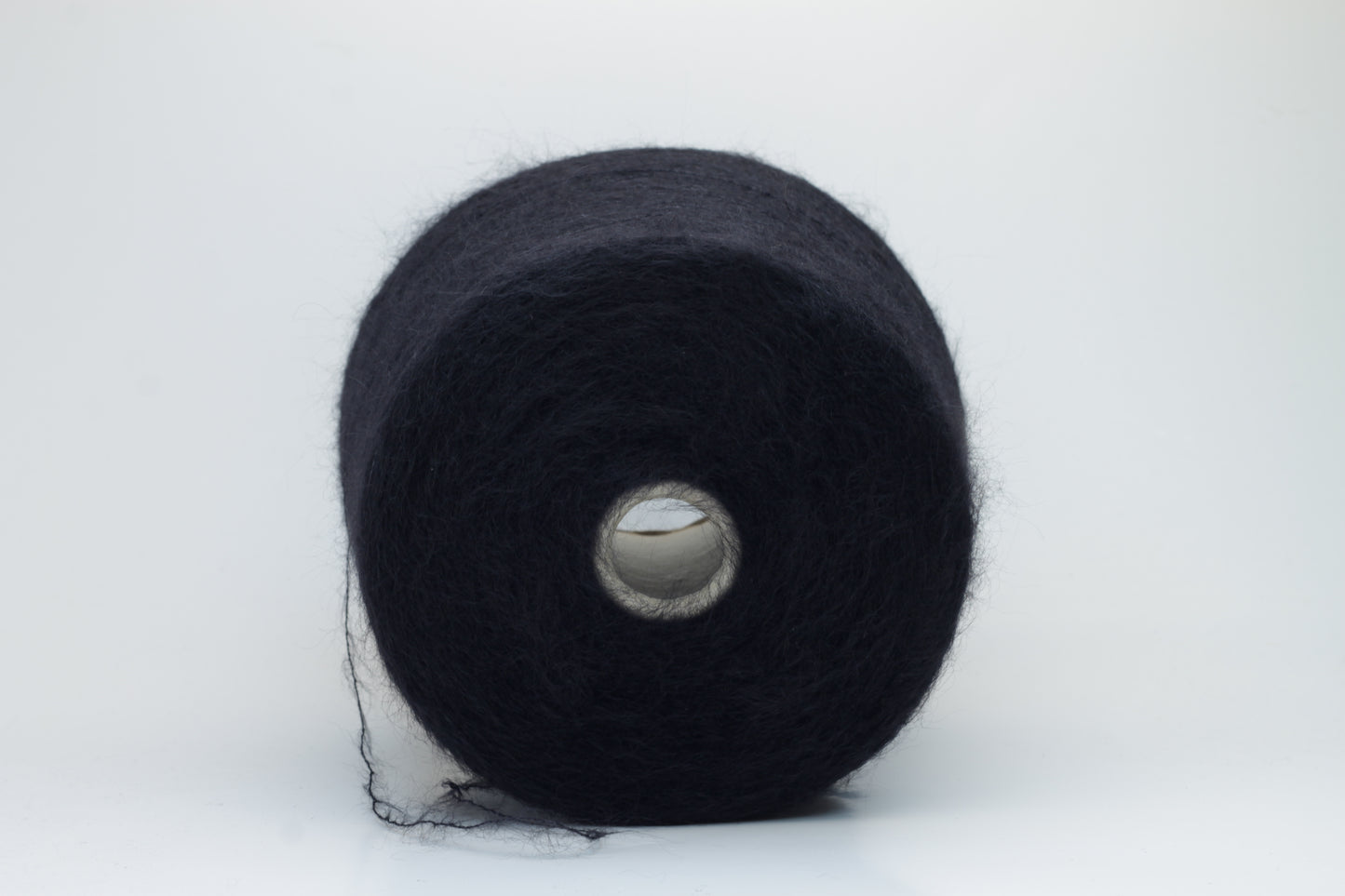 Close-up of fluffy Black kid mohair and silk blend yarn, subtly lustrous with a soft halo, gently twisted into a fine, delicate thread.
