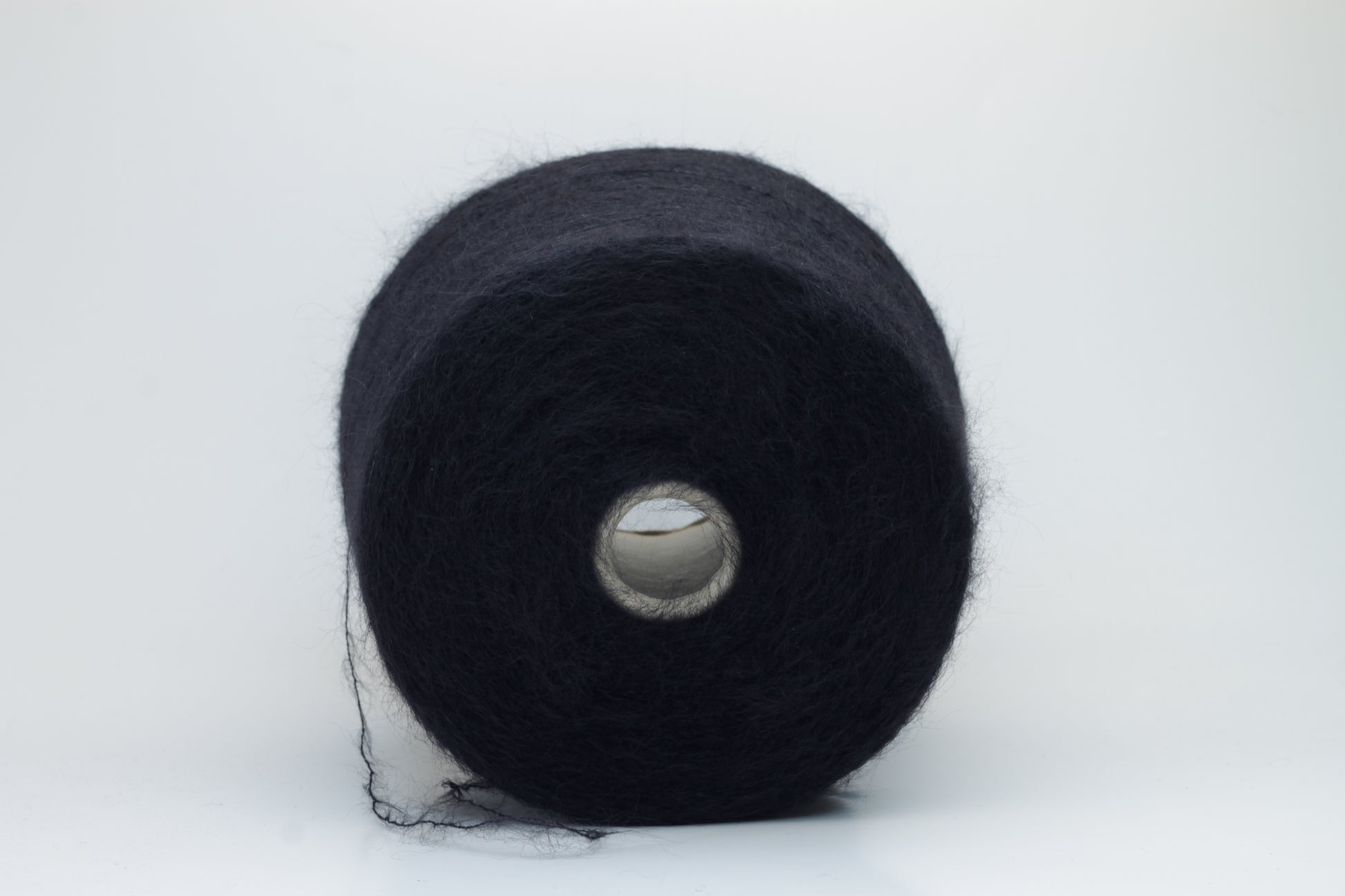 Close-up of fluffy Black kid mohair and silk blend yarn, subtly lustrous with a soft halo, gently twisted into a fine, delicate thread.