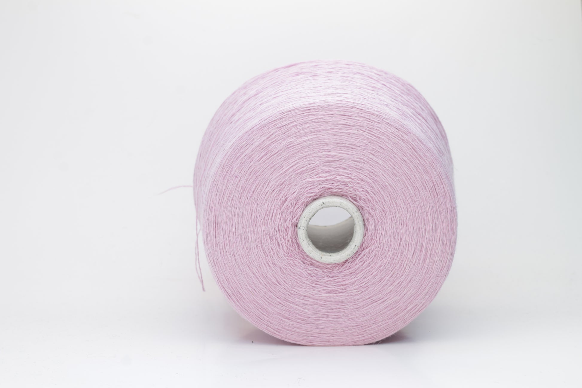 A soft, plump 2-ply yarn in a delicate antique rose hue, loosely coiled, exhibiting a subtle, silken sheen and slight halo. The fibers appear evenly spun.