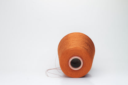 Close-up of a meticulously spun, single-ply bright orange silk yarn with a crisp, almost translucent quality and brilliant sheen.