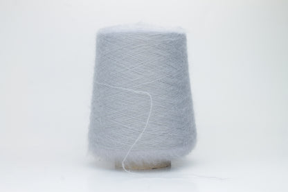 Close-up of fluffy Fumo Perla kid mohair and silk blend yarn, subtly lustrous with a soft halo, gently twisted into a fine, delicate thread.