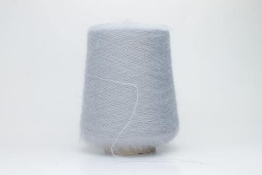 Close-up of fluffy Fumo Perla kid mohair and silk blend yarn, subtly lustrous with a soft halo, gently twisted into a fine, delicate thread.