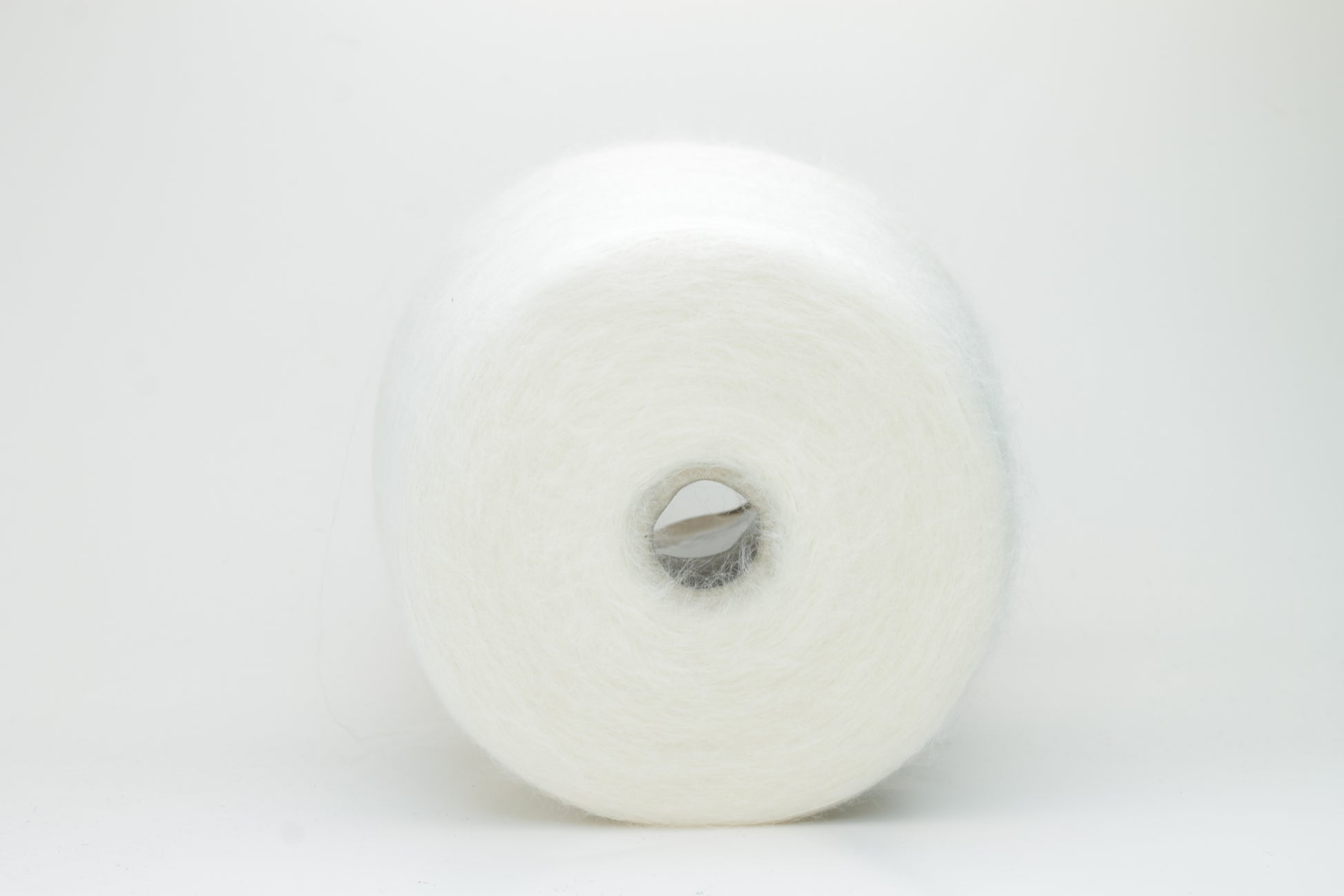 Close-up of fluffy white kid mohair and silk blend yarn, subtly lustrous with a soft halo, gently twisted into a fine, delicate thread.