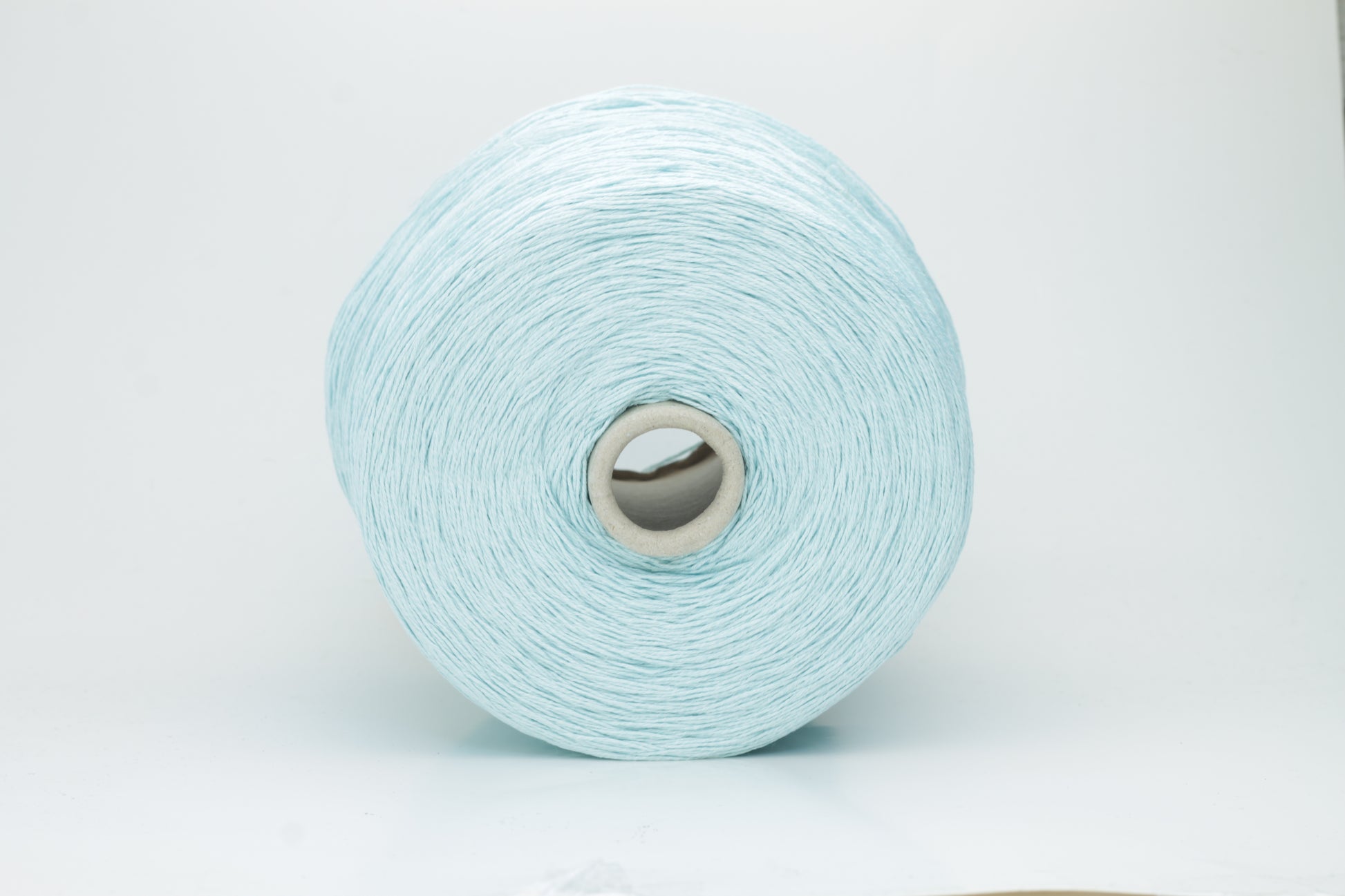 Close-up of fine, natural Linuzzo-colored 100% linen yarn, showing its smooth, slightly matte texture and subtle ply twist, coiled loosely.