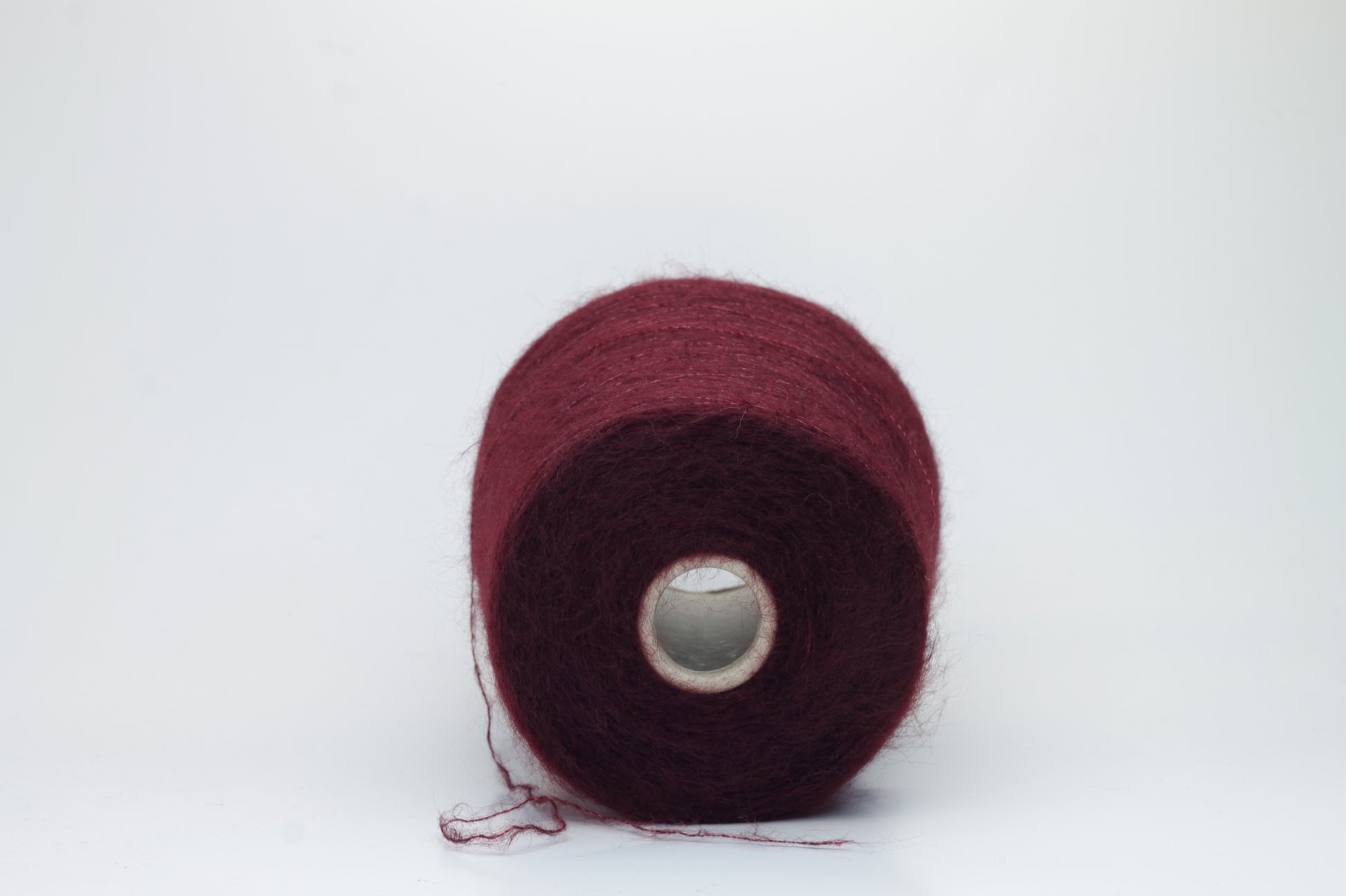 Close-up of fluffy Bordo kid mohair and silk blend yarn, subtly lustrous with a soft halo, gently twisted into a fine, delicate thread.
