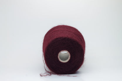 Close-up of fluffy Bordo kid mohair and silk blend yarn, subtly lustrous with a soft halo, gently twisted into a fine, delicate thread.