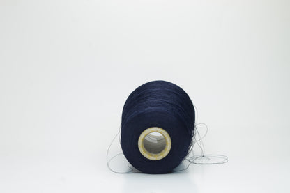 Close-up of a neatly wound spool of fine navy silk yarn, exhibiting a smooth, tightly twisted two-ply structure and a subtle, elegant sheen under direct light. The deep blue color appears rich and consistent.