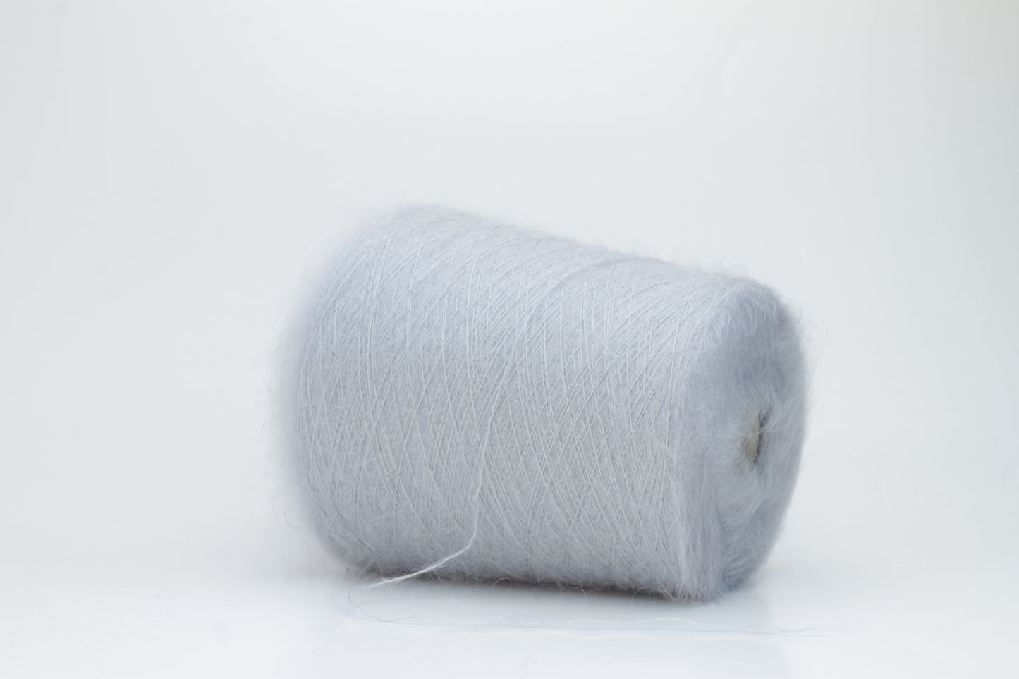 Close-up of fluffy Fumo Perla kid mohair and silk blend yarn, subtly lustrous with a soft halo, gently twisted into a fine, delicate thread.