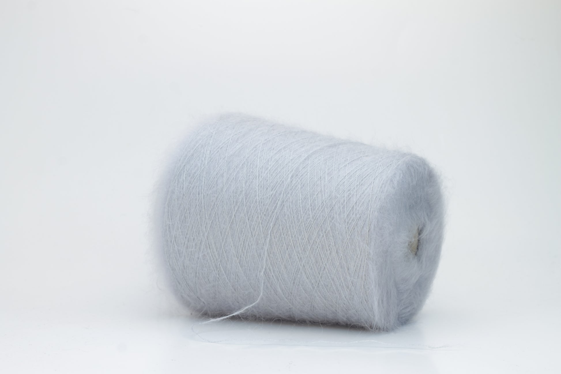 Close-up of fluffy Fumo Perla kid mohair and silk blend yarn, subtly lustrous with a soft halo, gently twisted into a fine, delicate thread.