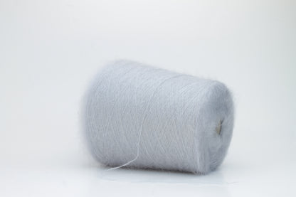 Close-up of fluffy Fumo Perla kid mohair and silk blend yarn, subtly lustrous with a soft halo, gently twisted into a fine, delicate thread.