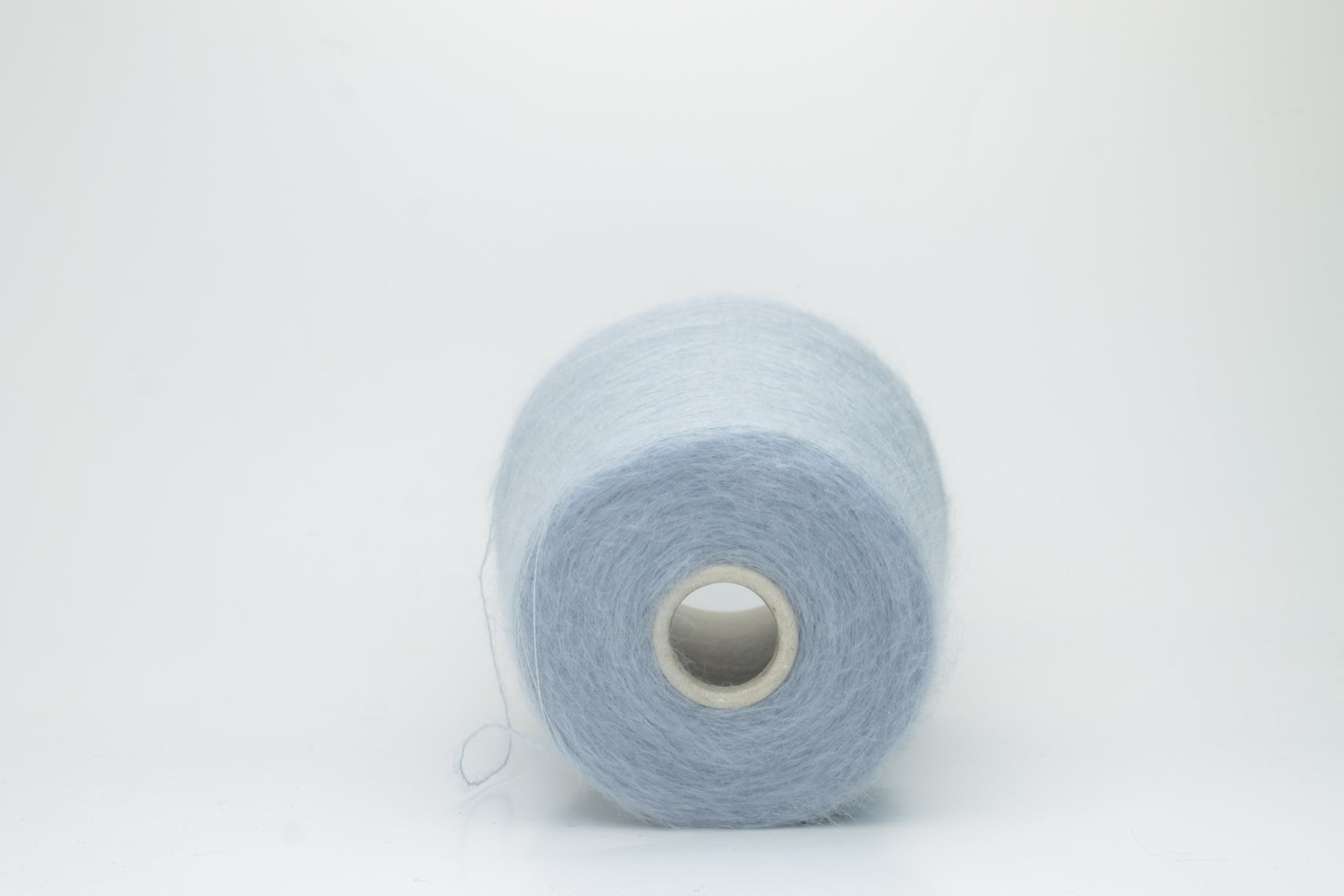 Close-up of fluffy Cielo kid mohair and silk blend yarn, subtly lustrous with a soft halo, gently twisted into a fine, delicate thread.