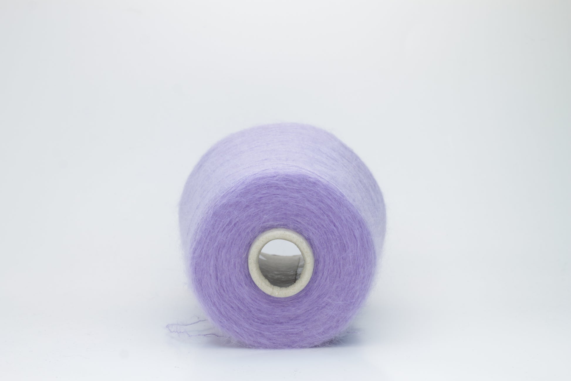 Close-up of fluffy Lila kid mohair and silk blend yarn, subtly lustrous with a soft halo, gently twisted into a fine, delicate thread.