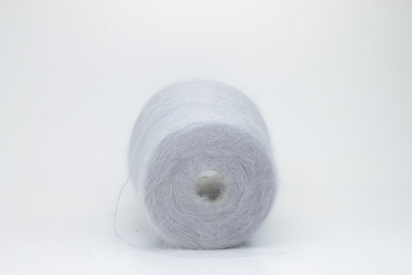 Close-up of fluffy Fumo Perla kid mohair and silk blend yarn, subtly lustrous with a soft halo, gently twisted into a fine, delicate thread.