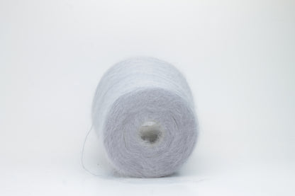 Close-up of fluffy Fumo Perla kid mohair and silk blend yarn, subtly lustrous with a soft halo, gently twisted into a fine, delicate thread.